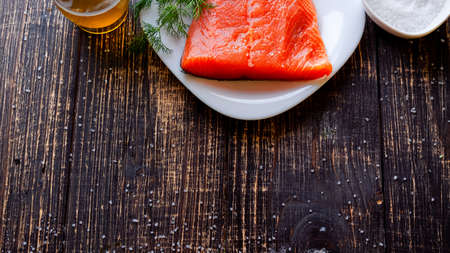 A piece of lightly salted salmon, salt and olive oil on a dark tableの写真素材