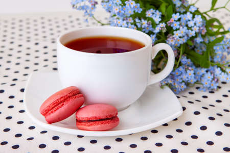 A cup of tea and tender strawberry macarons with a bouquet of wild forget-me-notsの写真素材