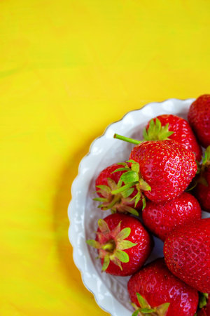 Ripe red sweet strawberry on a white plate on a yellow backgroundの写真素材