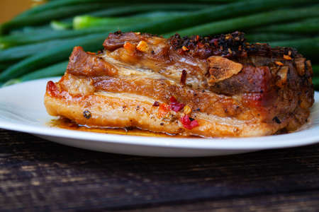 Spicy fried brisket with interlayers of pork bacon, baked with herbs and paprika, onion feathers in the backgroundの写真素材