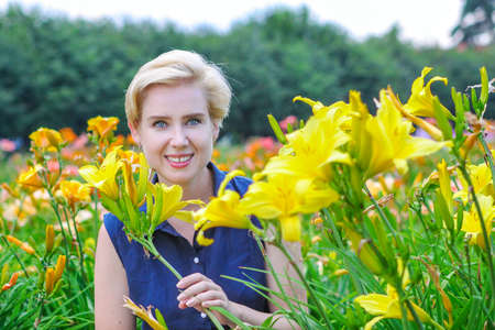 Blue-eyed blonde woman among lushly blooming yellow lilies in the gardenの写真素材
