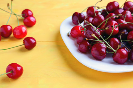 Fresh ripe cherries in a bowl with water drops, yellow background