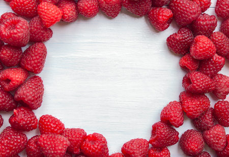 White background with fresh raspberries arranged in the shape of an oval frame on a wooden table