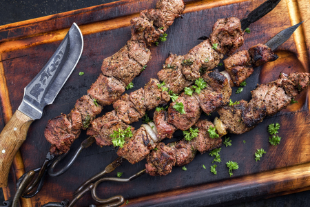 Traditional Russian shashlik on a barbecue skewer as a top view on an old burnt cutting boardの写真素材