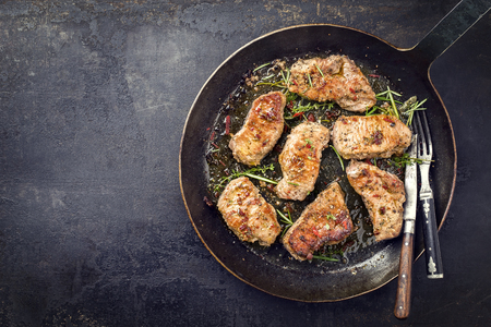 Fried saddle of pork steak with herb as top view in a frying pan with copy space left  の写真素材