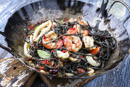 Italian linguine con tinta de calamari and prawns with olives as close-up on a wroth iron panの写真素材