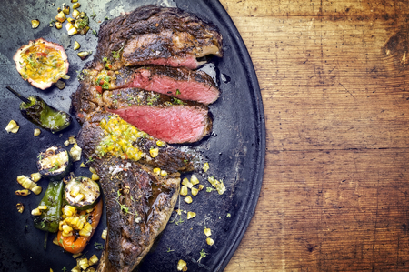 Australian barbecue dry aged wagyu tomahawk steak with vegetable and fruit relish as close-up on an old board の写真素材