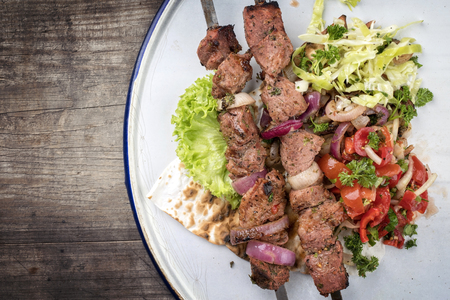Traditional Greek souvlaki barbecue skewer with cabbage and tomato onion salad as top view on phyllo bread with copy space leftの写真素材