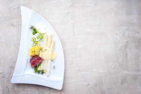 Modern barbecue dry aged sliced fillet steak with white asparagus in hollandaise sauce and roast potatoes as top view on a plate with copy space rightの写真素材
