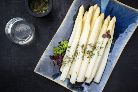 Traditional boiled white asparagus with wine as top view on a blue plateの写真素材