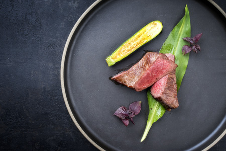 Traditional barbecue dry aged sliced fillet steak with wild garlic and baby zucchini as top view on a plate with copy spaceの写真素材