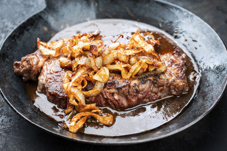 Traditional dry aged sliced roast beef with fried onion rings as closeup in a wrough-iron pan with brown sauceの写真素材