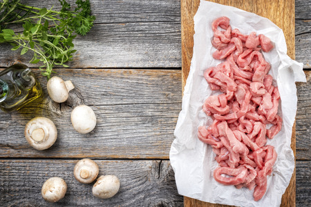Raw veal strips for traditional Swiss zurcher geschnetzeltes with herbs and mushrooms as closeup on a wooden cutting board with copy spaceの写真素材