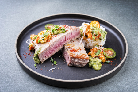 Traditional exotically tuna fish fillet with mango salsa and rice as closeup on a modern design black plateの写真素材