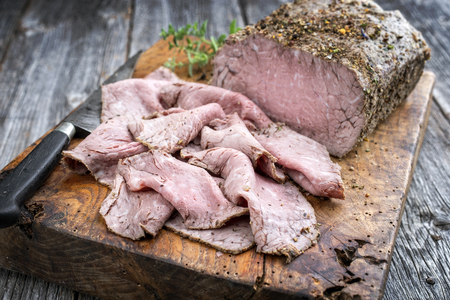 Traditional lunch meat with sliced cold cuts roast beef  as closeup on an old cutting boardの写真素材