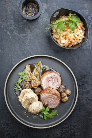 Traditional rolled boar roast with dumpling, fried vegetable and mushroom as top view on a modern design plate with game red wine sauceの写真素材