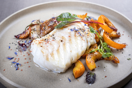 Fried Danish skrei cod fish filet with pumpkin, mushroom and lettuce as closeup on a modern design plate