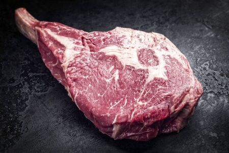 Raw dry aged angus tomahawk steak as top view on an old rustic board with copy spaceの写真素材
