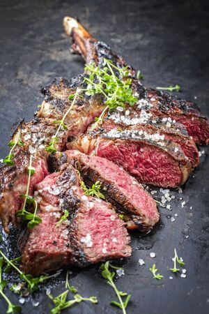 Traditional barbecue dry aged wagyu tomahawk steak sliced salt and herb as closeup on a rustic old black boardの写真素材