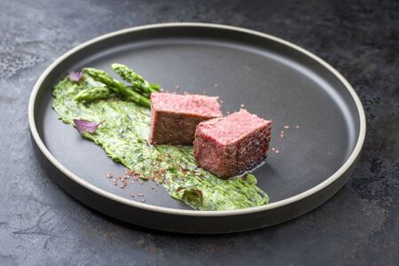 Blanched green asparagus with barbecue dry-aged wagyu fillet steak and avocado coriander relish as closeup on a modern design plateの写真素材