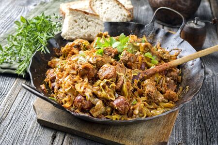 Traditional Polish kraut stew bigos with sausage, meat and mushrooms as closeup in a wrought-iron pan on an old wooden tableの写真素材