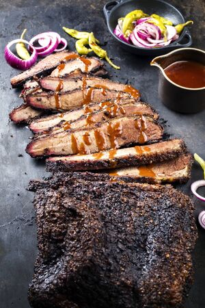 Traditional smoked barbecue wagyu beef brisket offered as closeup on an old rustic board with Louisiana sauce onion rings and peperoniの写真素材
