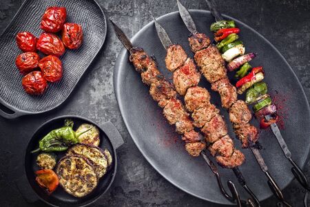 Traditional Russian shashlik on a barbecue skewer with vegetable and sumach paste as top view on a modern design plateの写真素材