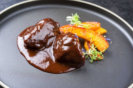 Traditional German braised beef cheeks in brown red wine sauce with pumpkin slices and herbs offered as closeup in a modern design plate の写真素材