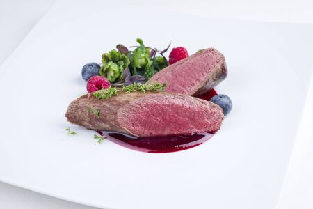 Fried dry aged venison tenderloin fillet medallion steak natural with kalette and raspberry sauce as closeup on a modern design plateの写真素材