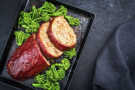 Traditional American meatloaf from ground beef with ketchup and broccoli as top view on a rustic metal tray with copy space の写真素材