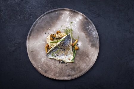 Gourmet fried gilthead fish filet with sliced dumpling, glasswort and algae as top view on a modern design plate with copy space の写真素材