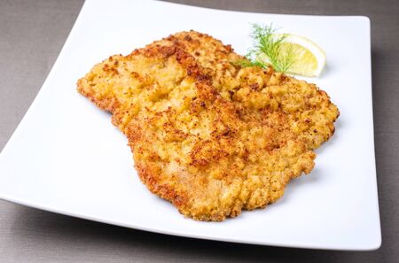 Traditional deep fried Wiener schnitzel from veal topside with lemon slice and herb offered as closeup modern design plateの写真素材