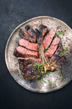 Barbecue dry aged wagyu porterhouse beef steak sliced with large fillet piece with herbs and red salt as top view on a modern design rustic plate with copy spaceの写真素材