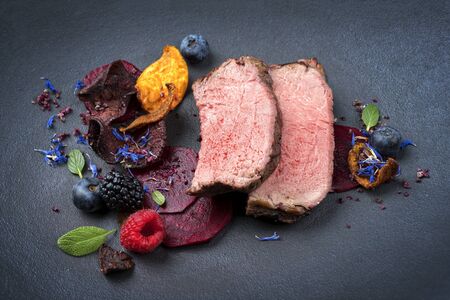 Barbecue dry aged wagyu roast beef natural sliced offered with vegetable chips and forest fruits as closeup on a modern design plateの写真素材