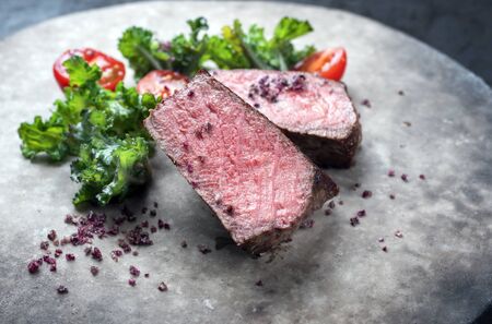 Barbecue dry aged wagyu roast beef natural sliced offered with rapini and tomatos as closeup on a modern design plateの写真素材