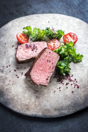 Barbecue dry aged wagyu roast beef natural sliced offered with rapini and tomatos as closeup on a modern design plateの写真素材