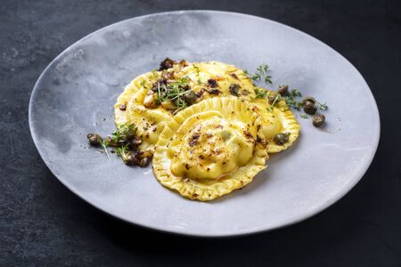 Traditional Italian ravioli pasta offered with capers and onion chili pesto closeup on a modern design plateの写真素材