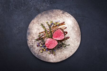 Barbecue dry aged beef fillet medallion steak natural with fried herbs and capers as top view on a modern design plate with copy space の写真素材
