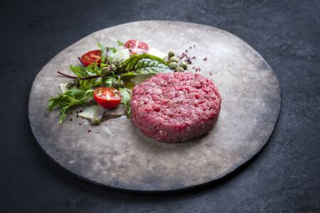 Gourmet tartar raw from beef fillet with lettuce, tomatoes and parmesan with capers as closeup on a rustic modern design plate with copy space の写真素材