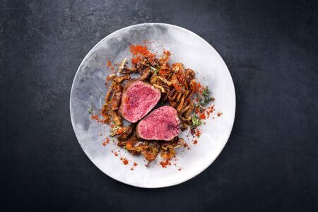 Barbecue dry aged beef fillet medallion steak natural with fried onion rings and carrots as top view on a modern design plate with copy space の写真素材