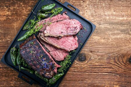 Traditional Commonwealth Sunday roast with sliced cold cuts roast beef with herbs and chili as top view on a modern design tray with copy space right の写真素材