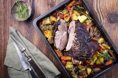 Traditional barbecue lamb roast sliced with tomatoes and fried potatoes as top view in a metal tray の写真素材