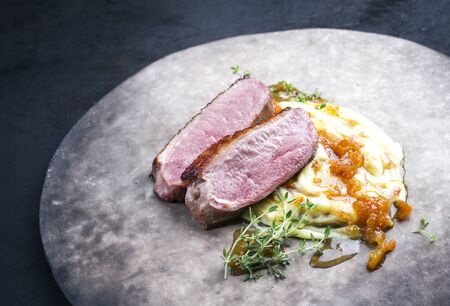 Traditional gourmet duck breast filet with mashed potatoes and orange sauce as closeup on a rustic modern design plate leftの写真素材