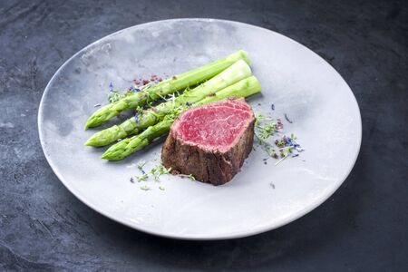 Barbecue dry aged wagyu beef fillet head medallion steak natural with green asparagus and herbs as closeup on a modern design plate with copy space の写真素材
