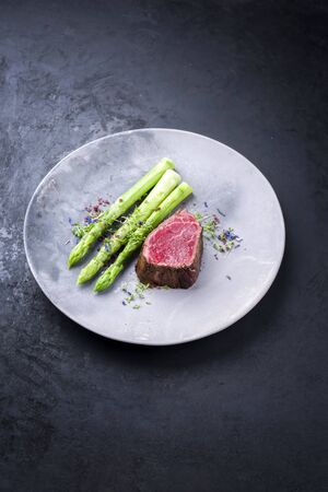 Barbecue dry aged wagyu beef fillet head medallion steak natural with green asparagus and herbs as closeup on a modern design plate with copy spaceの写真素材