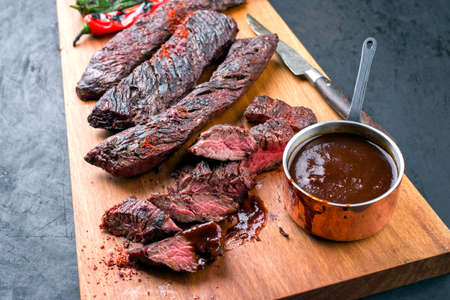 Barbecue wagyu skirt beef steak with hot chili and spice BBQ sauce offered as close-up on wooden design boardの写真素材