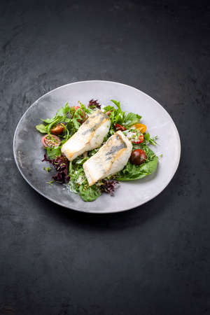 Traditional fried skrei cod fish filet with Italian lettuce and tomatoes in a lemon coconut sauce offered as top view in a modern design plate with copy spaceの写真素材