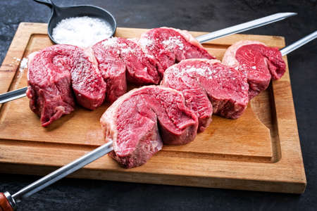 Raw dry aged wagyu picanha barbecue skewer from the cap of rump beef sliced and with salt offered as close-up on a wooden rustic cutting boardの写真素材
