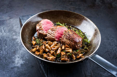 Fried dry aged beef fillet steak natural with king trumpet mushroom and herbs offered as close-up in a rustic frying panの写真素材