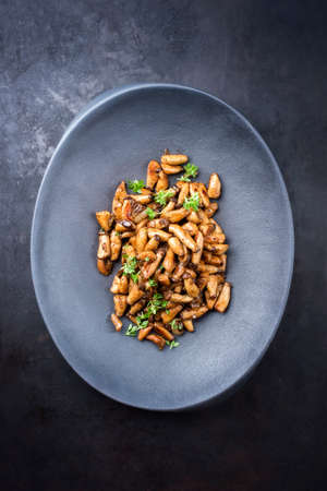 Traditional fresh fried baby king trumpet mushrooms with herbs offered as top view on a cast-iron design plateの写真素材